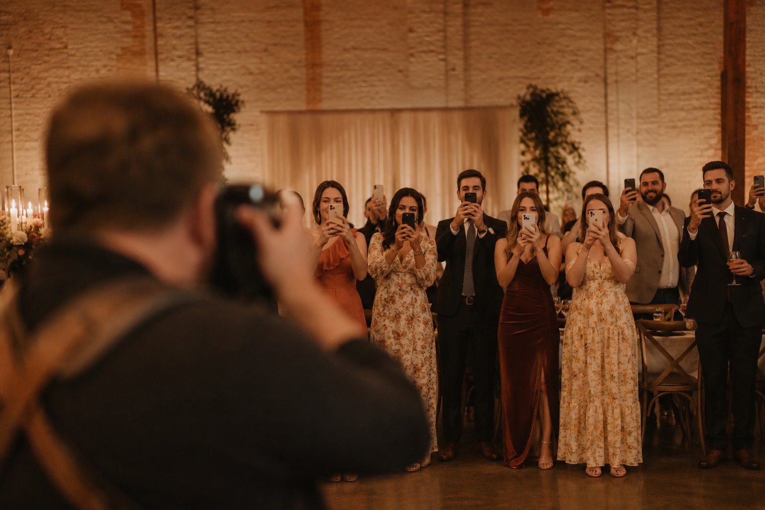 A wedding photographer in the foreground while a row of guests photograph the same moment on phones